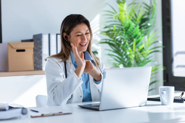 A doctor in a white coat smiling during a video consultation on a laptop